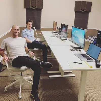 Two people sitting at a long desk in a sparse office with monitors.