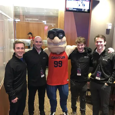 Four people in matching quarter-zips posing with a university sports mascot.