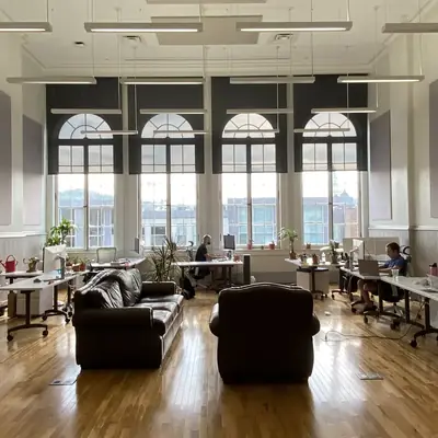 An open-plan office with tall arched windows, a few people working at desks.