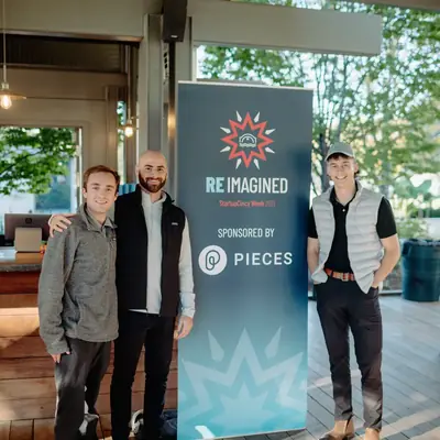 Four people standing beside a tall printed StartupCincy Week banner.