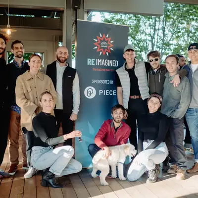 A group posed outdoors beside a RE:IMAGINED event banner, with a dog in front.