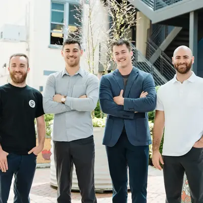 Four people posed outdoors in front of a building for a marketing photograph.