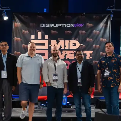 Five panellists standing on stage in front of a Disruption Now backdrop.